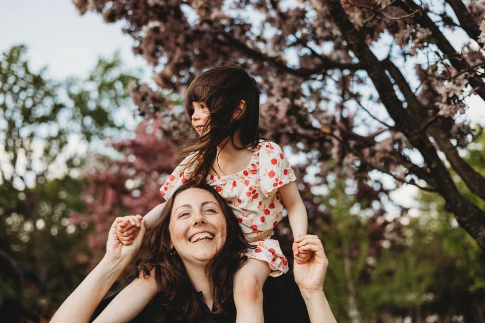 Photo fo mother with her young daughter on her shoulders in a park by Jenifer Blanco Monźon.