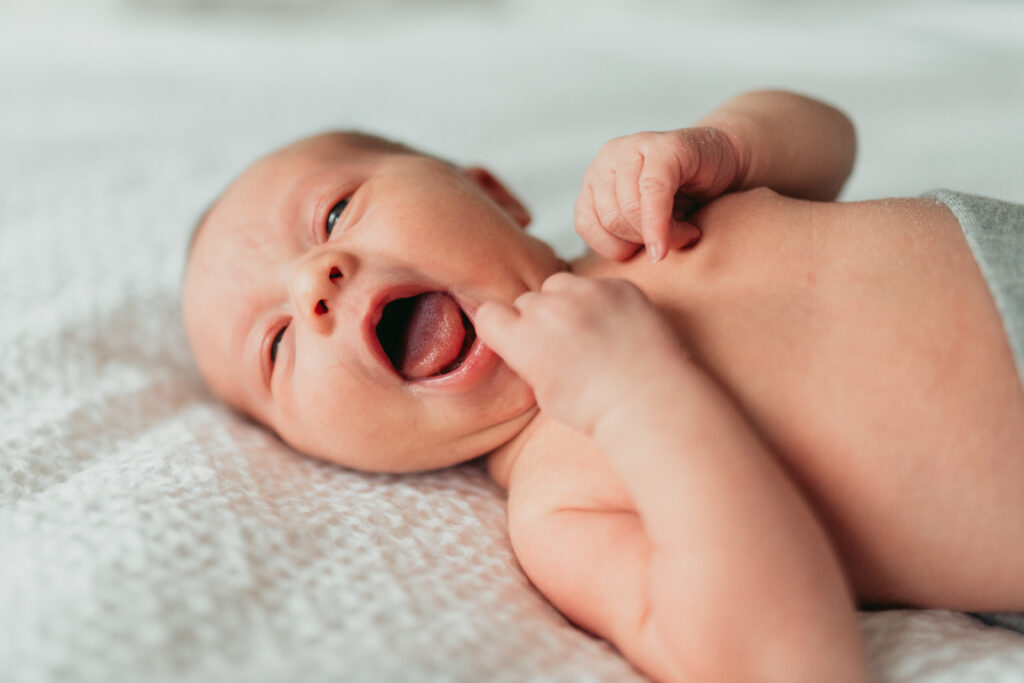 Happy smiling baby lays down on bed for a solo portrait.