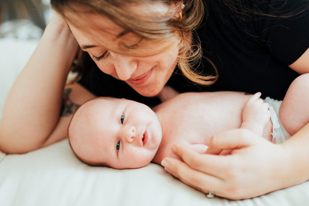 mother lovingly looks down at her new baby as they lay together on the bed.