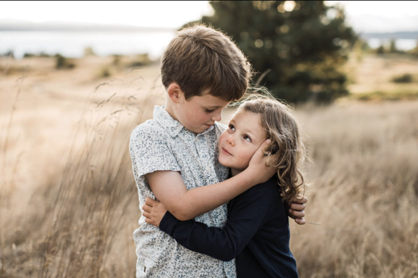 Siblings share a sweet hug in the golden grass field of Discovery Park Seattle.