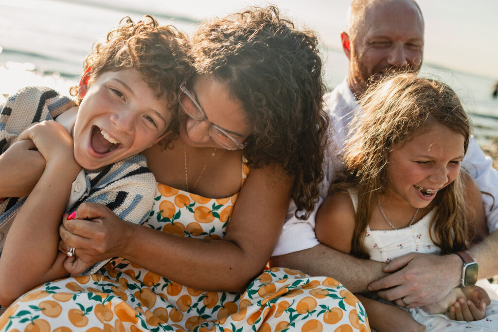 A family snuggled together on the beach at sunset, illustrating how clear directional posing creates authentic expressions for high-end family portraits.